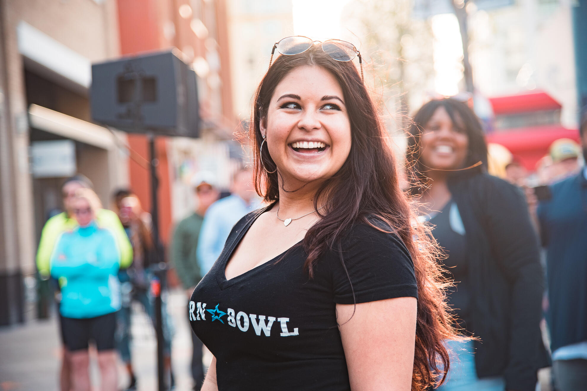 Smiling woman at outdoor community festival, captured in natural light with documentary style; vibrant crowd and city energy in background.